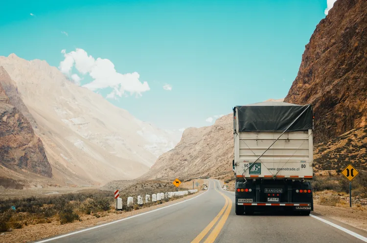 Caminhão baú trafegando por uma estrada de montanha, ilustrando o transporte de cargas documentado pelo CTe.